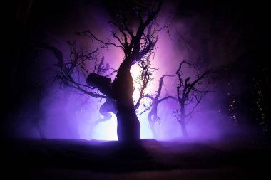 Ürkütücü karanlık manzara, sisli bir gecede bataklıktaki ağaç siluetlerini gösteriyor. Soğuk tonlarda gizemli bir orman. Dolunaya karşı ağaç dalları ve dramatik bulutlu gece gökyüzü