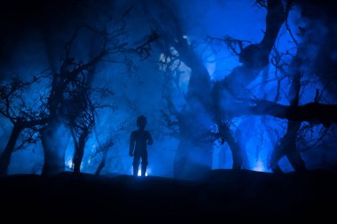 Karanlık ormanda duran bir insan silueti. Korku Cadılar Bayramı konsepti. Gecenin karanlığında ürkütücü bir ormanda tuhaf bir siluet.