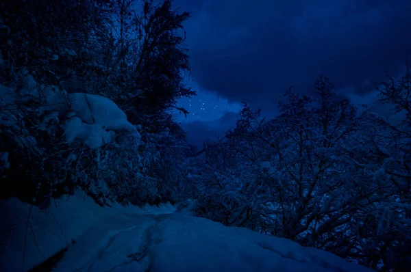 Mountain Road through the snowy forest on a full moon night. Scenic night winter landscape of dark blue sky with moon and stars. Azerbaijan