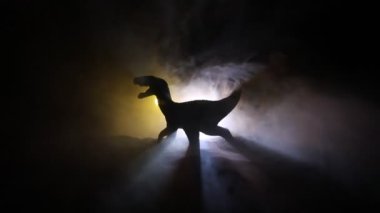 Sisli bir gecede duran T-Rex dinozor minyatürünün silueti. Renkli arka planlı sisli yaratıcı masa dekorasyonu. Seçici odak