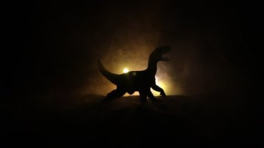 Sisli bir gecede duran T-Rex dinozor minyatürünün silueti. Renkli arka planlı sisli yaratıcı masa dekorasyonu. Seçici odak