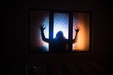 Kapalı cam bir kapıdan geçen, bilinmeyen bir gölge figürünün silueti. Geceleri pencerenin önündeki bir insanın silueti. Manyağın bulanık silueti korkunç cadılar bayramı konsepti.