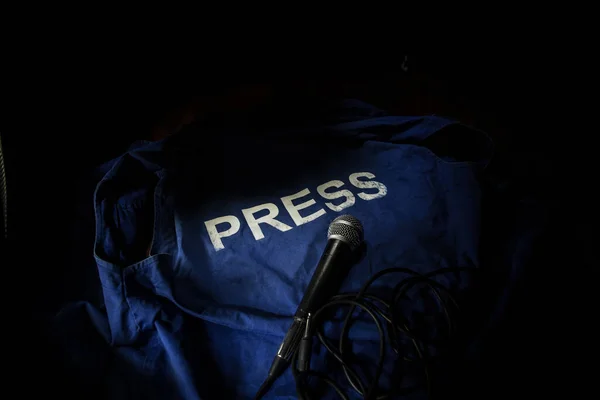 Media Journalism Global Daily News Content Concept. Blue journalist (press) vest in dark with backlight and fog. Media microphone on journalist vest. Selective focus