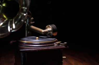 Müzik konsepti. Karanlık bir arka planda eski bir gramofon. Ahşap masanın üzerinde ton lambalı bir disk olan gramofon. Seçici odak
