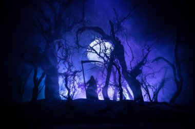 Karanlık sisli ormanda tırpanla ölüm. Ormanda Azrail 'i tutan kadın hayalet, cadılar bayramı konsepti. Seçici odak içindeki yaratıcı sanat tablosu dekorasyonları