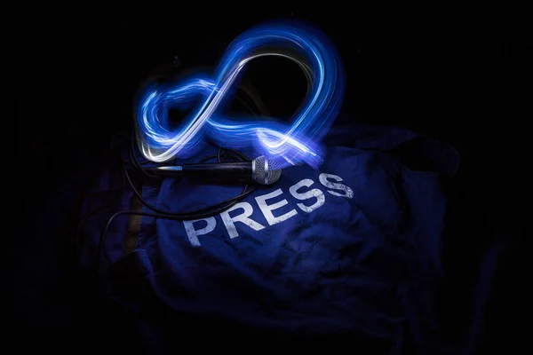 Media Journalism Global Daily News Content Concept. Blue journalist (press) vest in dark with backlight and fog. Media microphone on journalist vest. Selective focus