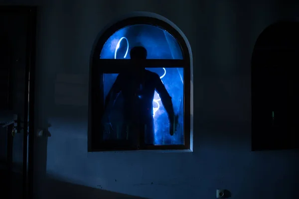 Silhouette of an unknown shadow figure on a door through a closed glass door. The silhouette of a human in front of a window at night. Scary scene halloween concept of blurred silhouette of maniac.