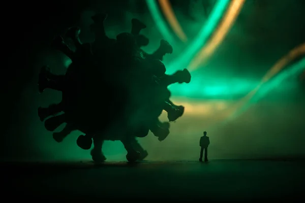 Corona virus global pandemic concept. Miniature man standing near big Corona virus novel in dark. Creative decoration with fog and backlight. Selective focus