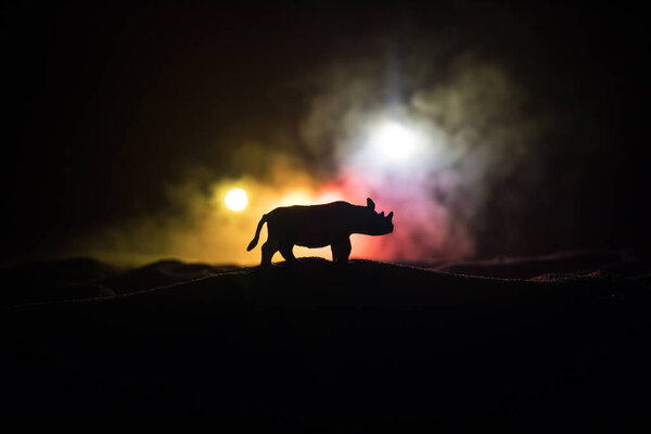 Силуэт миниатюры носорога, стоящей в туманную ночь. Креативное украшение стола цветной подсветкой с туманом. Селективный фокус