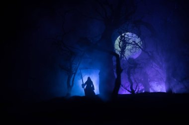 Karanlık sisli ormanda tırpanla ölüm. Ormanda Azrail 'i tutan kadın hayalet, cadılar bayramı konsepti. Seçici odak içindeki yaratıcı sanat tablosu dekorasyonları