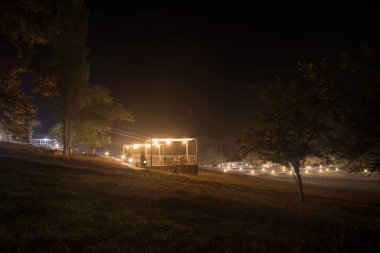 Geceleri ışık / çardağı olan bir çardak / gece parlayan bir çardak ya da sisli bir gecede ağaçlar ve sokak lambaları. Ormandaki boş yolda sisli gece lambaları.