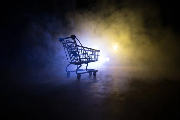 Empty shopping trolley on dark toned foggy background with some copy space. Financial crisis concept. Selective focus