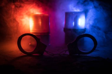 Gece polis baskını ve sen tutuklusun. Puslu arka planda yanıp sönen kırmızı ve mavi polis ışıkları olan kelepçelerin silueti. Seçici odak