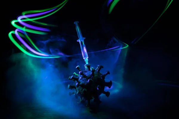 Corona virus Vaccine concept with syringe and green Corona virus novel miniature. Vaccine Concept of fight against coronavirus. Creative decoration with fog and backlight. Selective focus