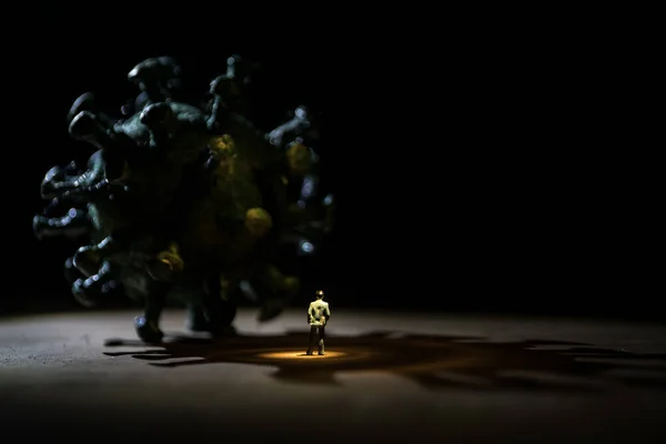 Corona virus global pandemic concept. Miniature man standing near big Corona virus novel in dark. Creative decoration with fog and backlight. Selective focus