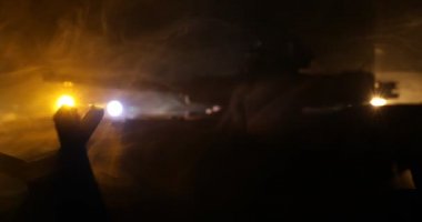 Zırhlı araç siluetinin savaş sisli arka planındaki savaş sahnesinin gece görüntüleri.
