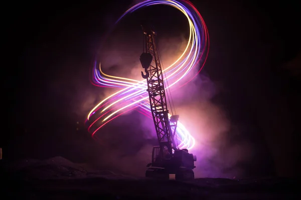 Abstract Industrial background with construction crane silhouette over amazing night sky with fog and backlight. Tower crane against the foggy sky at night. Industrial skyline. Selective focus