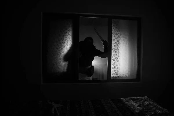 Silhouette of an unknown shadow figure on a door through a closed glass door. The silhouette of a human in front of a window at night. Scary scene halloween concept of blurred silhouette of maniac.