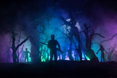 Zombi saldırısına karşı silahlı bir adam. Zombi kıyameti. Ormandaki bulanık zombilerin korkunç görüntüsü ve sisli, ürkütücü bulutlu gökyüzü. Korku Cadılar Bayramı konsepti.