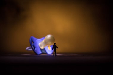 Yaratıcı bir kavram. Erkek silueti, ahşap masanın üzerinde yumuşak tonlu arka planda duran dev bebek emziğinde duruyor. Seçici odak