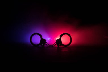 Gece polis baskını ve sen tutuklusun. Arka tarafında polis arabası olan kelepçelerin silueti. Görüntü sisli arka planda yanıp sönen kırmızı ve mavi polis ışıkları. Seçici odak