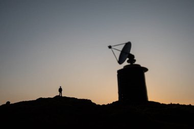 Yaratıcı sanat dekorasyonu. Gün batımında dev hava savunma radar anteninin yanında duran bir adamın silueti. Akşam gökyüzüne karşı uydu anteni ya da radyo anteni. Seçici odak