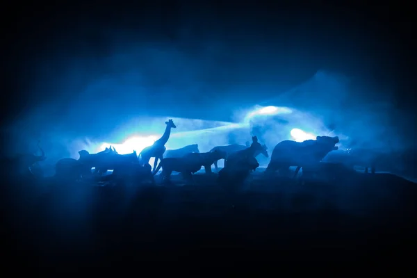 A group of animals are grouped together at foggy night with burning colorful background. Animals Running Escaping to Save Their Lives from fire. Selective focus.