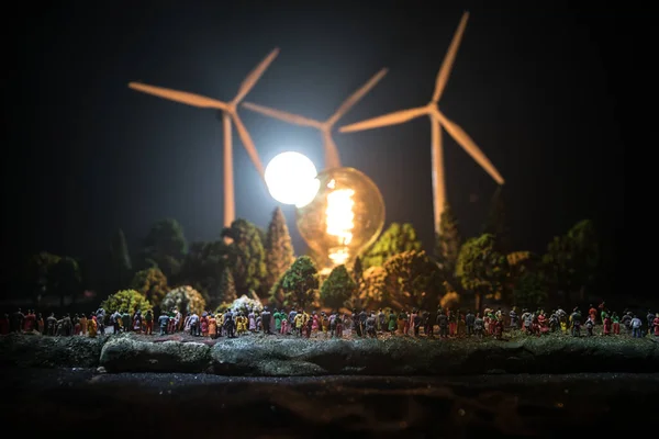 Electricity power in nature or clean energy concept. Wind Turbine producing alternative energy at night. Glowing bulb powered by alternative energy. Creative decoration with small miniature. Selective focus