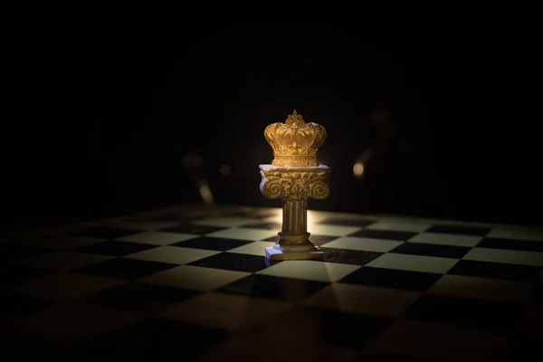 Beautiful queen/king crown on chessboard. chess board game concept of business ideas and competition and strategy ideas concept. Chess figures on a dark background with smoke and fog. Selective focus