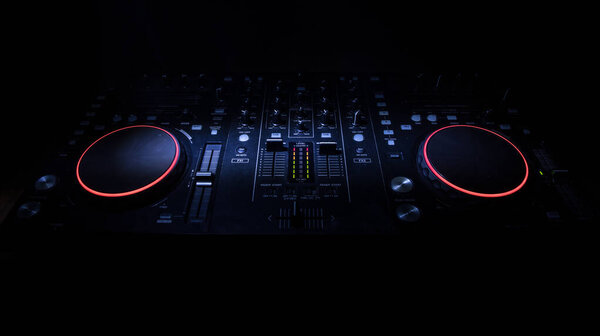 Club music concept. DJ console deejay-mixing desk in dark with colorful light. Mixer equipment entertainment DJ station. Selective focus