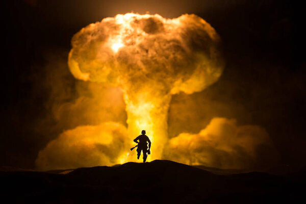 Nuclear war concept. Explosion of nuclear bomb. Creative artwork decoration in dark. Silhouette of soldier standing against giant mushroom cloud of atomic explosion. Selective focus