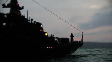 Savaş konsepti. Denizde gece savaşı sahnesi. Dramatik tonlu bulut etkisi. Gün batımında savaş gemisinin silueti. Minyatür yaratıcı masa dekorasyonu. Seçici odak