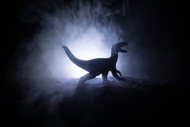 Sisli bir gecede dev dinozorun silueti. Küçük minyatür yaratıcı dekorasyon. Yanan sisli bir arka plan. Seçici odak