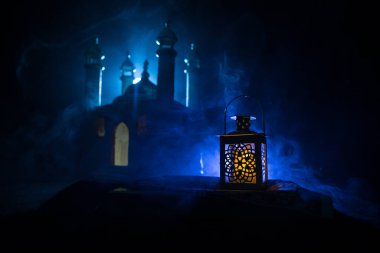 Gece parlayan yanan mumlu süs Arap feneri. Arka planda gerçekçi bir cami minyatürü var. Kutlama kartı, Müslüman kutsal ayı için davetiye Ramazan Kareem. Seçici odak