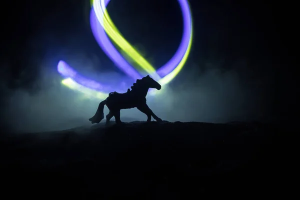 霧の夜に馬のミニチュア立ってシルエット 霧とカラフルなバックライトと創造的なテーブルの装飾 選択的焦点 — ストック写真