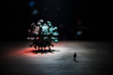 Corona virüsü küresel salgın konsepti. Karanlıkta büyük Corona virüsü romanının yanında duran minyatür adam. Sis ve arka ışıklandırmalı yaratıcı dekorasyon. Seçici odak