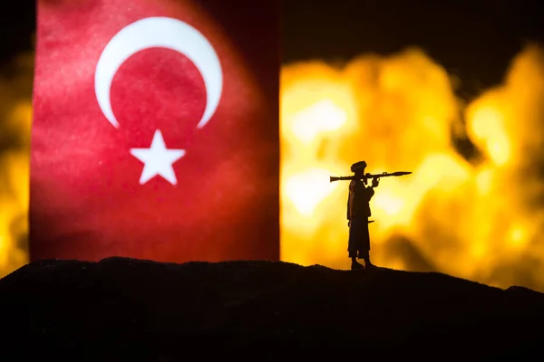Turkey small flag on burning dark background. Concept of crisis of war and political conflicts between nations. Silhouette of armed soldier against a Turkish flag. Selective focus