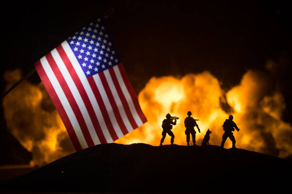 Маленький флаг США на горящем темном фоне. Концепция кризиса войны и политических конфликтов между народами. Силуэт вооруженного солдата против флага США. Селективный фокус