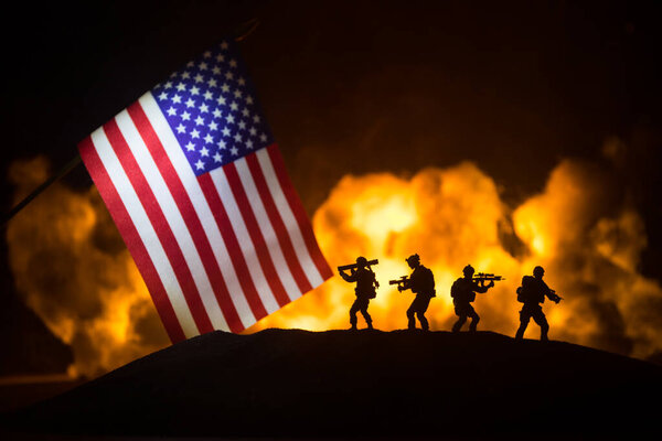 Маленький флаг США на горящем темном фоне. Концепция кризиса войны и политических конфликтов между народами. Силуэт вооруженного солдата против флага США. Селективный фокус
