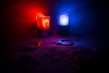Gece polis baskını ve sen tutuklusun. Puslu arka planda yanıp sönen kırmızı ve mavi polis ışıkları olan kelepçelerin silueti. Seçici odak
