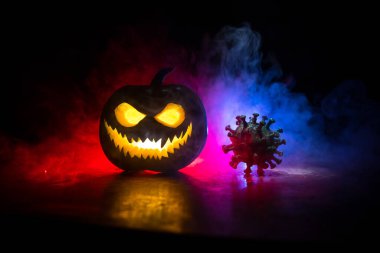 Corona virüsü küresel pandemik konsepti sırasında Cadılar Bayramı. Karanlıkta parlayan balkabakları ve Covid romanı tematik ürkütücü süslemelerle. Cadılar Bayramı balkabağı sisli arka planda. Seçici odak