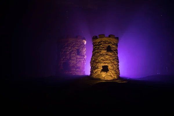 Stone defence tower at night. Medieval castle miniature with toned foggy backlight. Creative table decoration. Selective focus