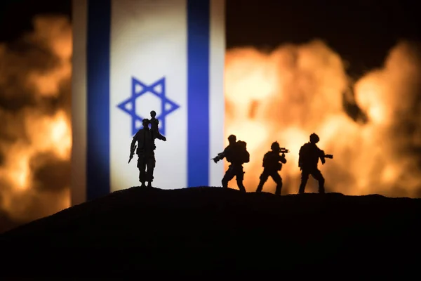 Israel small flag on burning dark background. Concept of crisis of war and political conflicts between nations. Silhouette of armed soldier against a Israel flag. Selective focus