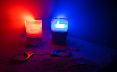 Gece polis baskını ve sen tutuklusun. Puslu arka planda yanıp sönen kırmızı ve mavi polis ışıkları olan kelepçelerin silueti. Seçici odak