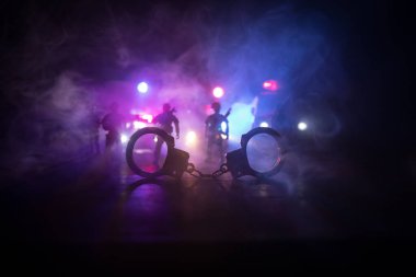 Gece polis baskını ve sen tutuklusun. Arka tarafında polis arabası olan kelepçelerin silueti. Görüntü sisli arka planda yanıp sönen kırmızı ve mavi polis ışıkları. Seçici odak