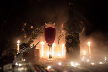 Noel süslemeli bir kadeh şarap. Kırmızı şarap kristal bardakta, renkli halıda şişe ve yaratıcı yeni yıl süslemeleri. Boşluğu kopyala