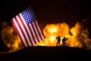 Yanan karanlık arka planda ABD bayrağı. Savaş krizi kavramı ve uluslar arasındaki siyasi çatışmalar. Amerikan bayrağına karşı silahlı asker silueti. Seçici odak