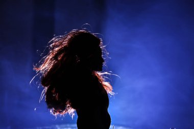 Hafif arka planda bir kadının silueti. Gece karanlığında uzun saçlı, sisli arka planda mavi ışıkları olan yalnız bir oyuncak bebek. Seçici odak