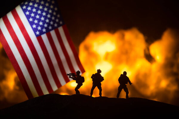 Маленький флаг США на горящем темном фоне. Концепция кризиса войны и политических конфликтов между народами. Силуэт вооруженного солдата против флага США. Селективный фокус