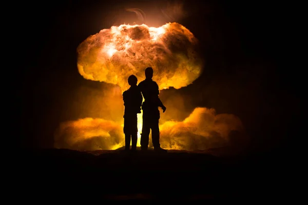 Nuclear war concept. Explosion of nuclear bomb. Creative artwork decoration in dark. Silhouettes of soldiers standing against giant mushroom cloud of atomic explosion. Selective focus